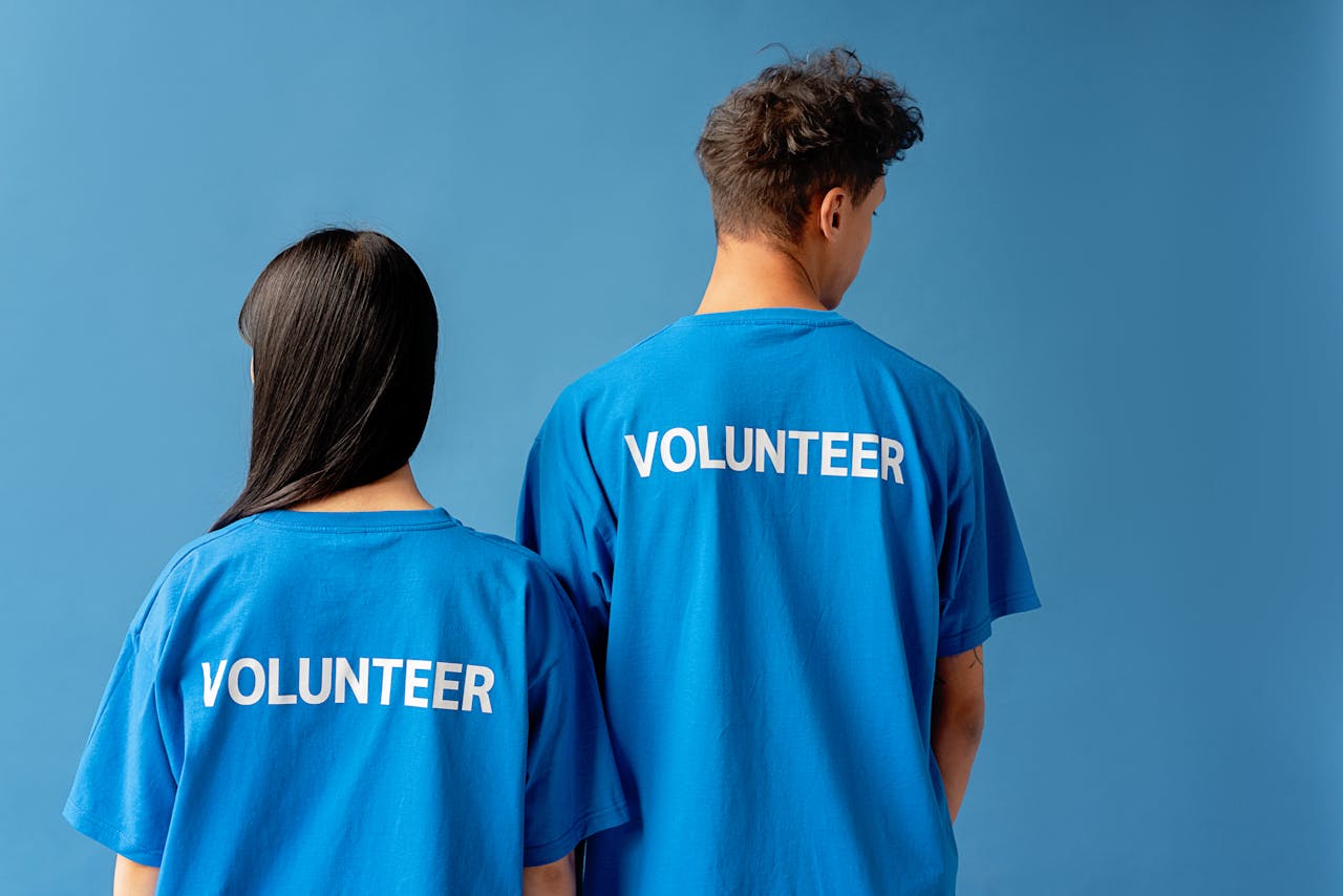 Two people wearing blue volunteer shirts standing against a blue background.